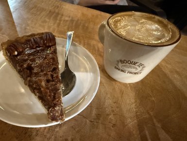 Ein Stück köstlicher Nusskuchen, garniert mit Pecannüssen, liegt auf einem weißen Teller neben einer dampfenden Kaffeetasse.