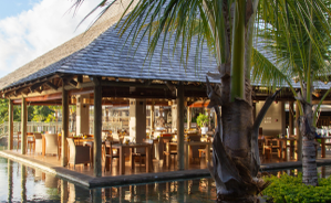 Ein stilvolles Restaurant mit Holzterrasse, umgeben von Palmen und einem glitzernden Pool, strahlt tropisches Flair aus.