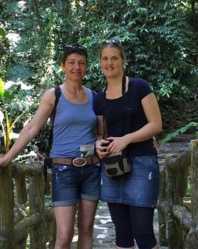 Zwei Frauen posieren lächelnd auf einem Holzsteg in einem üppigen, grünen Dschungel in Vietnam.