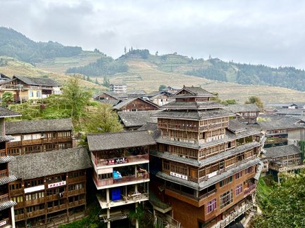 Blick auf traditionelle Holzhäuser in Longsheng, umgeben von terrassierten Reisfeldern und sanften Hügeln.