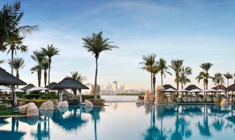 Ein luxuriöser Poolbereich umgeben von Palmen und Liegen, mit Blick auf die Skyline von Dubai im Hintergrund.