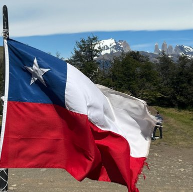 Die chilenische Flagge weht vor einer beeindruckenden Berglandschaft mit schneebedeckten Gipfeln im Hintergrund.