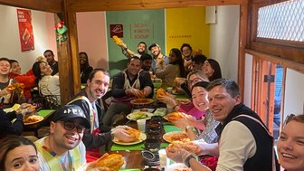 Eine Gruppe von Menschen sitzt an einem Tisch und hält stolz ihre selbstgemachten Kimchi-Teile in den Händen.