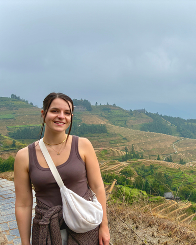 Eine junge Frau steht lächelnd vor den beeindruckenden Reisterrassen in Longsheng, umgeben von grünen Hügeln.