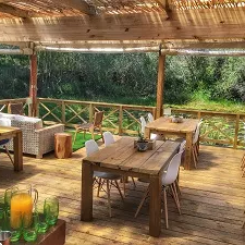 Ein einladender Restaurantbereich mit Holztischen und Stühlen, umgeben von üppiger Natur und einem Blick auf das Grün.