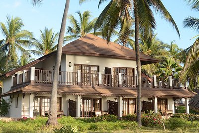 Ein elegantes Gebäude mit einem Balkon, umgeben von hohen Palmen und üppigem Grün, strahlt tropische Entspannung aus.