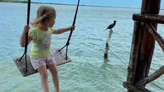 Kind schaukelt über dem smaragdgrünen Wasser mit Blick auf die Lagune – Mexiko Familienreise