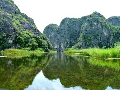 Eine ruhige Wasseroberfläche spiegelt die majestätischen, bewaldeten Felsen und das üppige Grün der Umgebung wider.