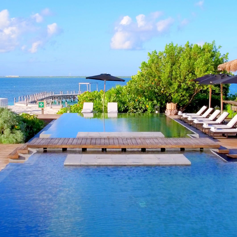 Ein luxuriöser Poolbereich mit Liegen und Sonnenschirmen, umgeben von üppigem Grün und Blick auf das Meer.