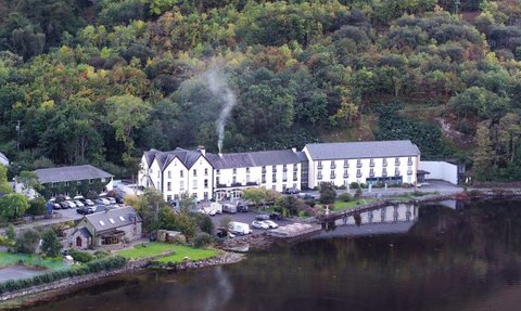 Ein malerisches Hotel am Ufer eines ruhigen Sees, umgeben von üppigem, grünem Wald und sanften Hügeln.