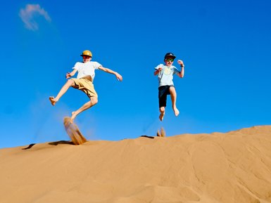 Kinder genießen die Freiheit und springen voller Freude auf den weiten Sanddünen der Wüste – Marokko Reise mit Kindern