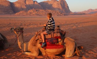 Kind sitzt beim Sonnenuntergang auf einem Kamel - Jordanien mit Kindern