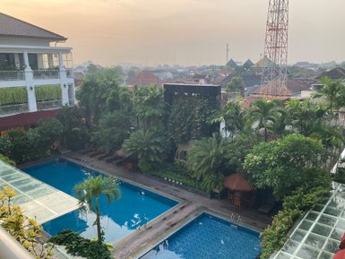 Ein Blick auf einen ruhigen Hotelpool, umgeben von üppigem Grün und Sonnenliegen, unter einem sanften Morgenhimmel.