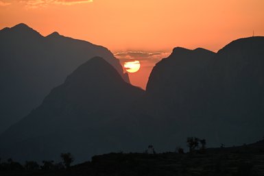 Die letzten Sonnenstrahlen tauchen die Schluchten und Gipfel des Jebel Shams in warmes Licht – Oman Reise mit Kindern