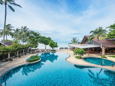 Ein einladender Pool mit blauen Fliesen, umgeben von Palmen und Liegen, bietet einen Blick auf das ruhige Meer.