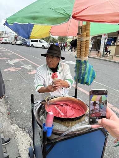 Ein Straßenverkäufer bereitet frisches Eis in einer bunten Verkaufsbude unter einem großen Regenschirm zu.