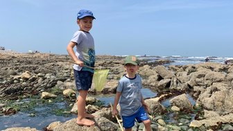 Zwei Kinder spielen zwischen Felsen am Strand - Namibia mit Jugendlichen