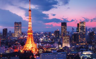 Der Tokyo Tower leuchtet in warmen Farben, während die Stadt unter einem dramatischen Abendhimmel erstrahlt.