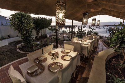 Ein stilvolles Restaurant mit Tischen, die für ein romantisches Abendessen am Wasser vorbereitet sind, umgeben von Pflanzen.