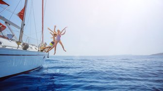 Drei Kinder springen fröhlich von einer Yacht ins glitzernde blaue Wasser, umgeben von einem klaren Himmel.