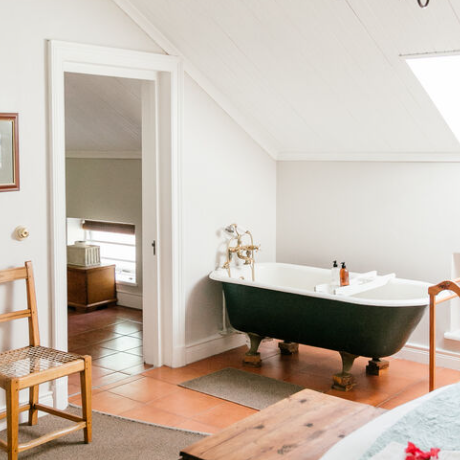 Ein helles Badezimmer mit einer freistehenden Badewanne, einem Holzstuhl und einem großen Fenster, das Tageslicht hereinlässt.