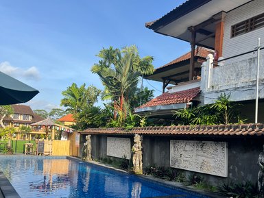 Ein glitzernder Pool spiegelt den blauen Himmel wider, umgeben von üppigem Grün und balinesischer Architektur.