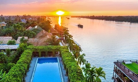 Ein atemberaubender Sonnenuntergang über dem Mekong, mit einem Pool und üppiger Vegetation im Vordergrund.