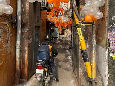 Ein Motorradfahrer fährt durch eine enge Gasse, geschmückt mit orangefarbenen und transparenten Luftballons.