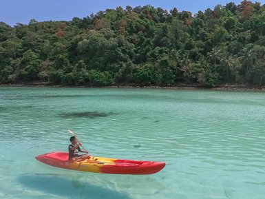 Erwachsener fährt in Kanu über kristallklares Wasser auf Inselparadies Koh Talu - Thailand mit Kindern