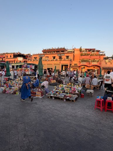 Lebendige Szenerie auf dem Djemaa el-Fnaa Platz in Marrakesch mit Ständen und Menschen in traditionellen Kleidern.
