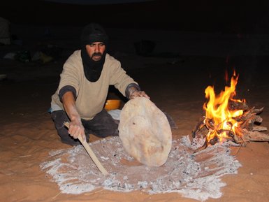 Beduine backt traditionelles Fladenbrot direkt auf dem Wüstensand – Marokko Familienreise