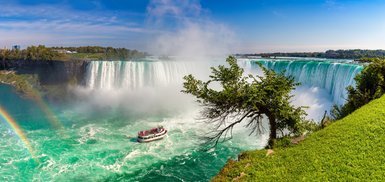 Die Niagarafälle stürzen majestätisch in den türkisfarbenen Fluss, während ein Boot mit Touristen in der Nähe fährt.