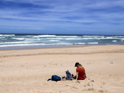 Kind sitzt mit Mutter im Sand und schaut aufs Meer – Garden Route Familienreise