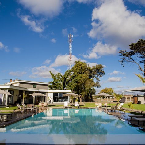 Ein klarer Pool spiegelt den blauen Himmel und die Wolken wider, umgeben von Liegen und Sonnenschirmen in einer ruhigen Umgebung.