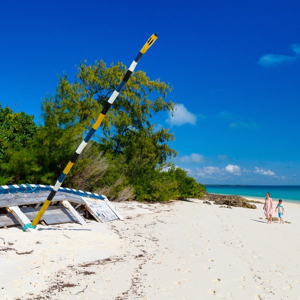 Ein verlassenes Boot liegt auf dem weißen Sandstrand, während eine Familie am Ufer entlang spaziert und die Sonne genießt.