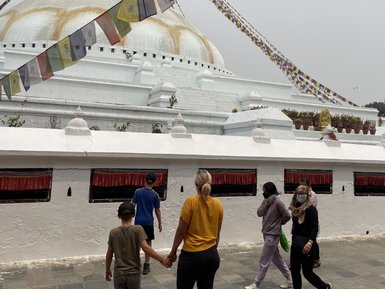 Eine Familie mit zwei Kindern erkundet den Bodhnath Stupa, umgeben von bunten Gebetsfahnen und einer spirituellen Atmosphäre.