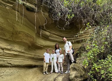 Eine Familie steht in einer beeindruckenden, geschichteten Felslandschaft, umgeben von üppigem Grün und hängenden Pflanzen.