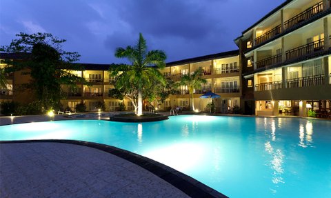 Ein beleuchteter Pool umgeben von Palmen und einem Hotel, das in der Dämmerung eine entspannende Atmosphäre schafft.