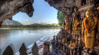 Der Blick aus einer Höhle zeigt eine Vielzahl von Buddha-Statuen, die am Ufer eines ruhigen Flusses stehen.