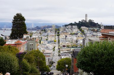 Eine malerische Aussicht auf die hügelige Stadt San Francisco mit bunten Häusern und dem Wasser im Hintergrund.