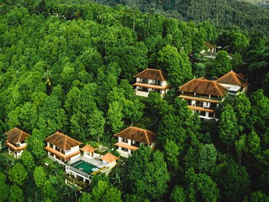 Eine Luftaufnahme zeigt mehrere Villen, umgeben von üppigem, grünem Wald, die Ruhe und Naturverbundenheit ausstrahlen.