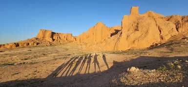 Lange Schatten von Menschen fallen auf die sandige Landschaft der Flaming Cliffs, umgeben von beeindruckenden Felsformationen.