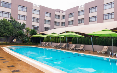 Ein einladender Poolbereich mit grünen Sonnenschirmen und Liegen, umgeben von einem modernen Hotel in Nairobi.