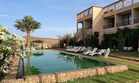 Ein klarer Pool spiegelt den Himmel und die umgebenden Palmen wider, während lounge-Bereiche einladend wirken.