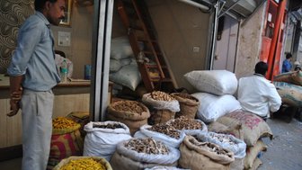 Ein Mann steht neben einem Stapel von Säcken mit verschiedenen Gewürzen in einem geschäftigen Markt in Delhi.