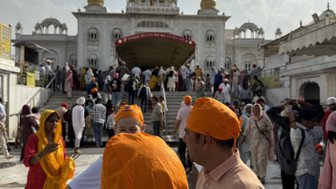 Eine Gruppe von Menschen mit orangefarbenen Turbanen versammelt sich vor dem Gurudwara Bangla Sahib, das prächtig im Hintergrund steht.