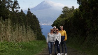 Eine Gruppe von vier Personen posiert lächelnd auf einem Weg, umgeben von üppiger Natur und einem Vulkan im Hintergrund.