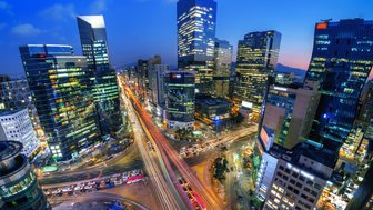 Die Stadt Seoul erstrahlt in der Dämmerung, mit leuchtenden Wolkenkratzern und lebhaften Straßen voller Autos.