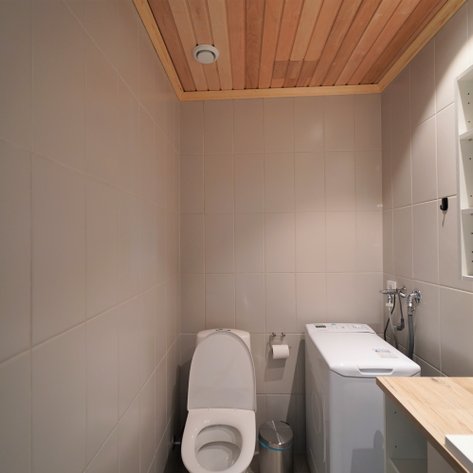 Ein modernes Badezimmer mit einer weißen Toilette, einer Waschmaschine und einem Holzregal an der Wand.