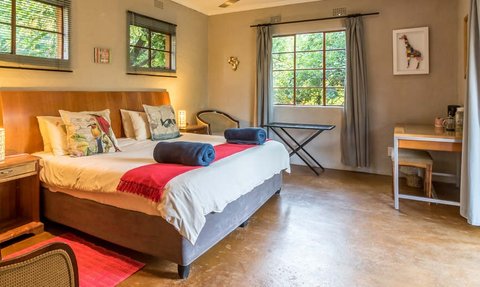 Ein gemütliches Zimmer mit einem großen Bett, bunten Kissen und einem Fenster, das auf eine grüne Landschaft blickt.